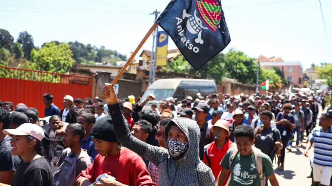 يحمل أحد المتظاهرين لافتة عليها نسخة مدغشقرية من شعار المانغا اليابانية الشهيرة ون بيس، وهو رمز تبنته حركات الاحتجاج بين جيل زد في جميع أنحاء العالم، بينما يسير مع متظاهرين آخرين خلال مظاهرة وطنية بقيادة الشباب احتجاجًا على انقطاع التيار الكهربائي المتكرر ونقص المياه، في أنتاناناريفو، مدغشقر، 13 أكتوبر/تشرين الأول 2025.