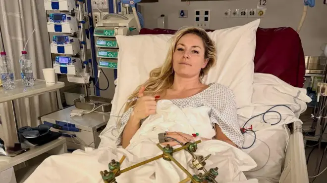 Линдси Вонн в больничной койке делает знак рукой, поднимая большой палец.