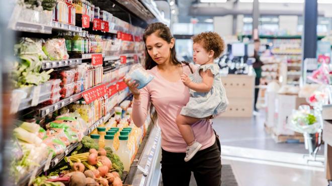 Uma mãe segurando a filha e olhando os preços dos produtospixbet aposta futebolum supermercado