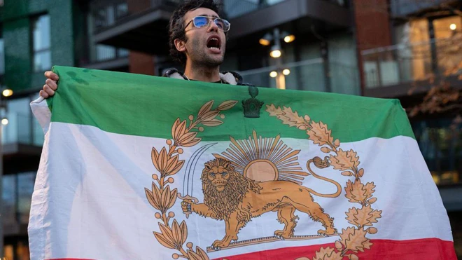 Протестующий что-то кричит, держа в руках старый военно-морской флаг Ирана - со львом и солнцем