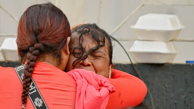 Una mujer con una camiseta manga larga roja abraza a otra mujer, que llora desconsolada. 