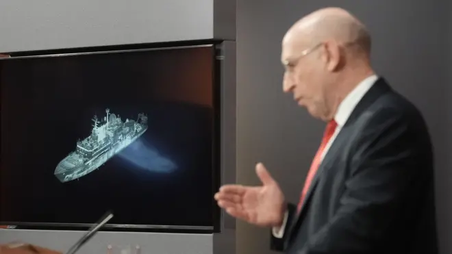 John Healey at a lectern with a picture of the Yantar behind