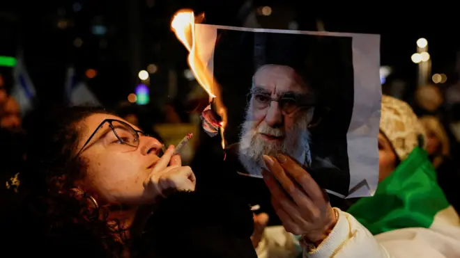 Una mujer enciende un cigarrillo con fuego de una imagen en llamas del líder supremo de Irán, el ayatolá Ali Khamenei.