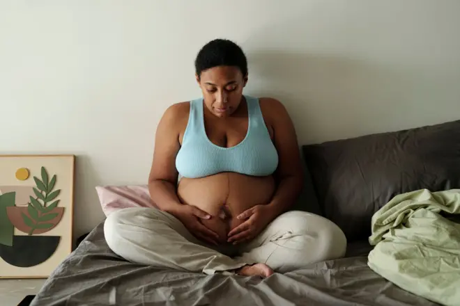 A pregnant woman sitting on the bed placed her hands below her bump