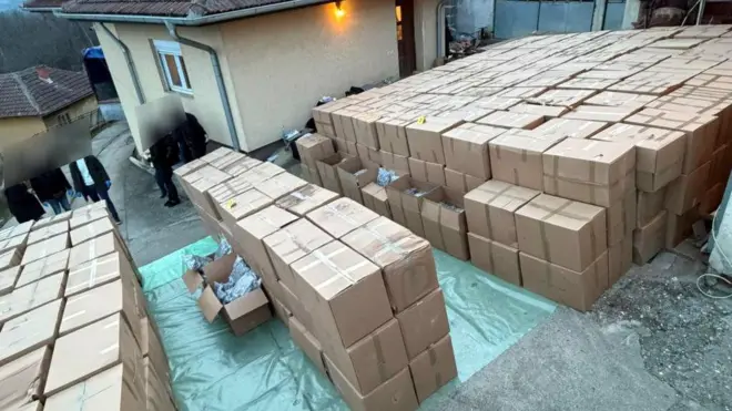 Desetine kutija ispred kuće i nekoliko ljudi čija su lica zamagljena