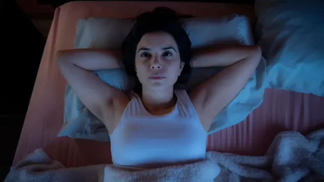 Woman lying awake in bed at night staring at ceiling 