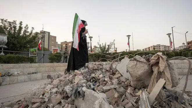 İranlı bir kadın, Tahran'da yıkıntıların üzerinde elinde İran bayrağıyla yürüyor - 21 Haziran 2025