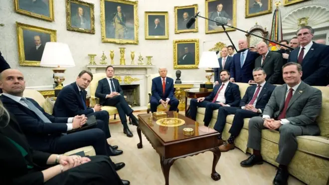 Assessores de Trump sentados próximos ao presidente, com quadros ao fundo.