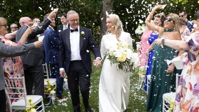 Australian Prime Minister Anthony Albanese and Jodie Haydon walk down the aisle towards the camera. Guests throw confetti over the couple