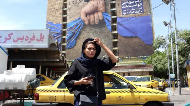 An Iranian woman walks near a huge billboard referring to the Strait of Hormuz and words reading in Persian 'Forever in Iran's hand' at Vanak square in Tehran, Iran, 06 May 2026.