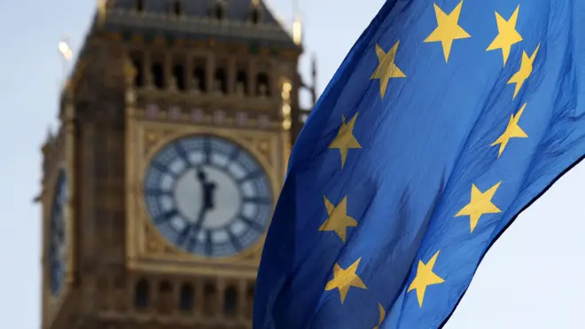Foto do Big Ben com a bandeira da União Europeia no primeiro plano. 
