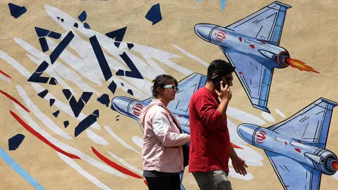 تمرّ امرأة ورجل بجانب جدارية مناهضة للولايات المتحدة وإسرائيل في طهران في 21 أبريل 2026، في ظلّ وقفٍ لإطلاق النار في المنطقة. ومع اقتراب انتهاء وقفٍ لإطلاق النار استمرّ أسبوعين، قالت البيت الأبيض إن نائب الرئيس الأمريكي مستعد للعودة إلى باكستان لإجراء مفاوضات جديدة بهدف إنهاء الصراع الذي أدى إلى ارتفاع أسعار النفط الخام وأعاد إشعال مخاوف التضخم