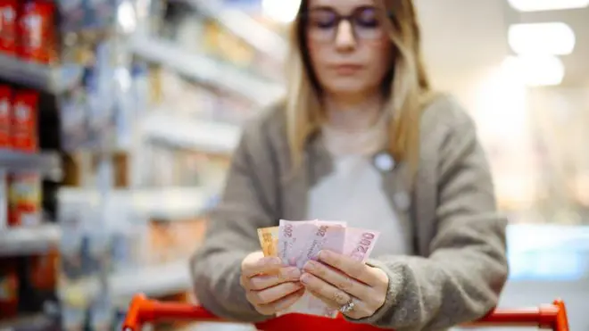 Bir kadın market arabasının üzerinden 200 TL'lik banknot tutuyor. 