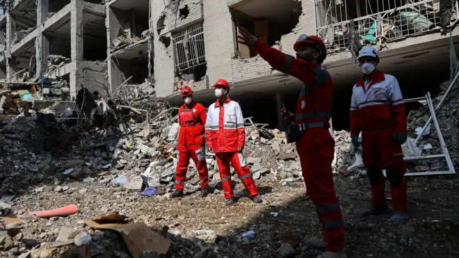 ईरान के तेहरान में हवाई हमले से क्षतिग्रस्त एक इमारत में रेड क्रिसेंट बचाव दल के सदस्य काम करते हुए