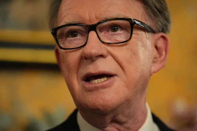 Peter Mandelson em retrato de rosto, com a boca aberta, usando óculos e uma camisa social branca