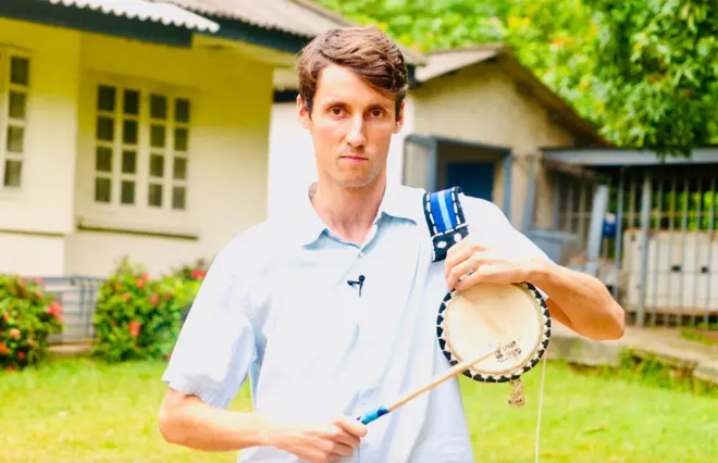 Ọkùnrin aláwọ̀funfun kan tó gbé ìlù dání tó sì ń wo ọ̀ọ́kán