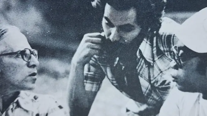 Foto em preto e branco mostra três homens conversando, com olhares compenetrados