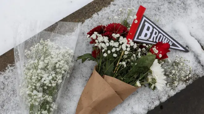 雪の積もった路上に、白いカスミソウの花束と、「BROWN」と書かれた大学のワッペンと紅白の花束が置かれている。 