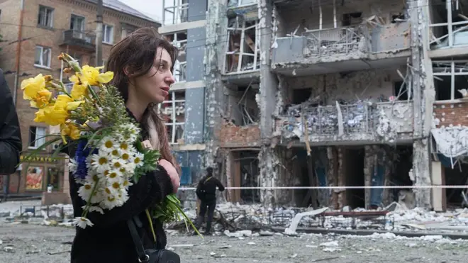 امرأة تحمل باقة من الزهور أمام مبنى سكني شاهق الارتفاع في منطقة متضررة بشدة جراء غارة روسية بطائرة بدون طيار في كييف في 25 مايو/ أيار 2025