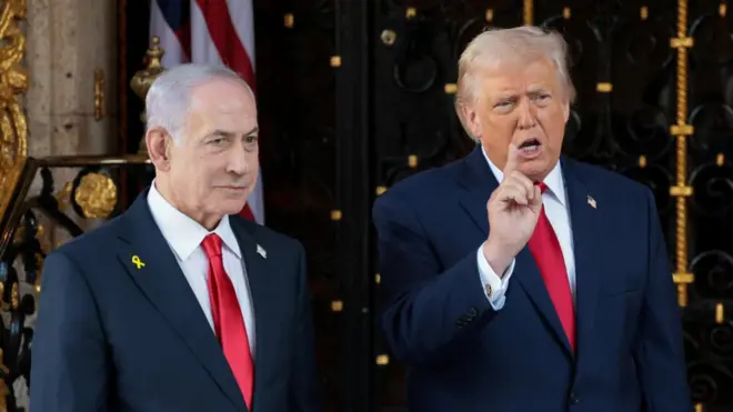 2人ともダークスーツに白シャツ、赤ネクタイ姿で、横並びに立っている。トランプ氏は右手を上げて人差し指を立てながら口を開いている