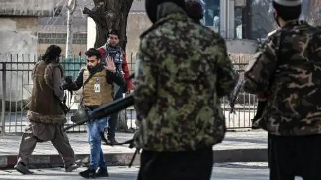 تصویر یک خبرنگار که به وسیله دو سرباز حکومت طالبان که یونیفرم نظامی بر تن و سلاح به دارند از کار بازداشته می شود.