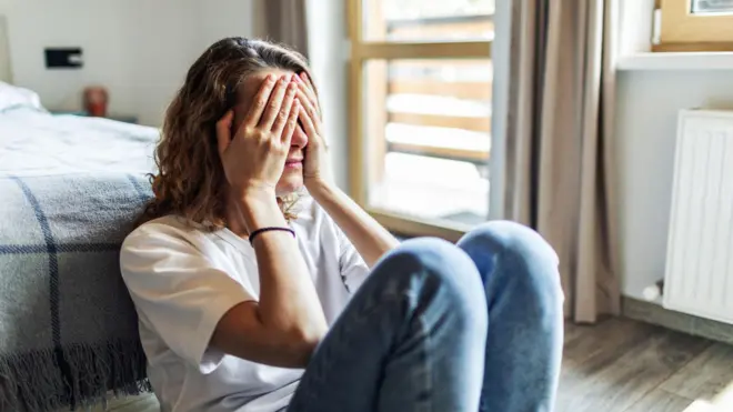 امرأة تغطي وجهها بيديها وتجلس على الأرض 