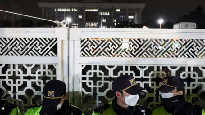 Police in caps, facemasks and high-viz jackets stand guard in front of the gate of the National Assembly after South Korea's president declared martial law