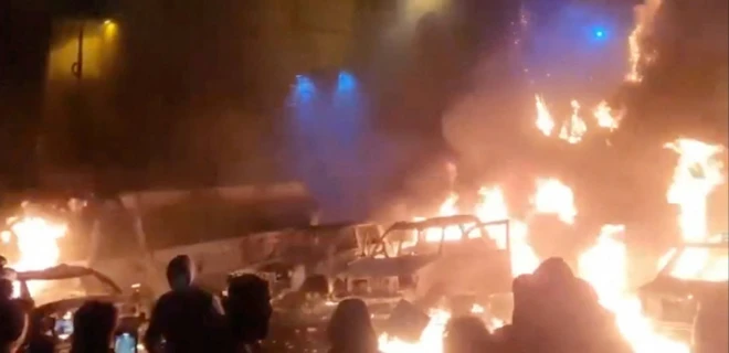 Fotoğrafta çok sayıda aracın yandığı anlar görülüyor. Araçlar barikat yapılır gibi sıralanmış ve bir grup gösterici oraya doğru bakıyor.