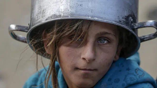 فتاة فلسطينية نازحة تحمل وعاءً فارغاً فوق رأسها تنتظر الحصول على طعام من مطبخ خيري في جباليا في شمال قطاع غزة، في 2 مايو/أيار 2025