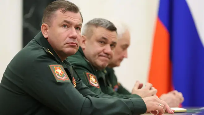 Два генерала и министр обороны на встрече с Путиным. Они сидят в форме за столом, на заднем плане — российский флаг.