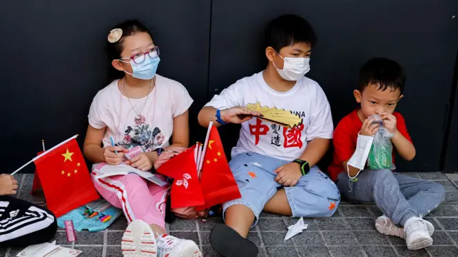 中共建政周年“十一国庆”香港一群小孩手持中国国旗与香港特区区旗坐在路旁休息（资料图片）