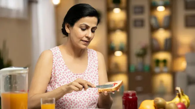 ब्रेडला जॅम लावताना एक महिला