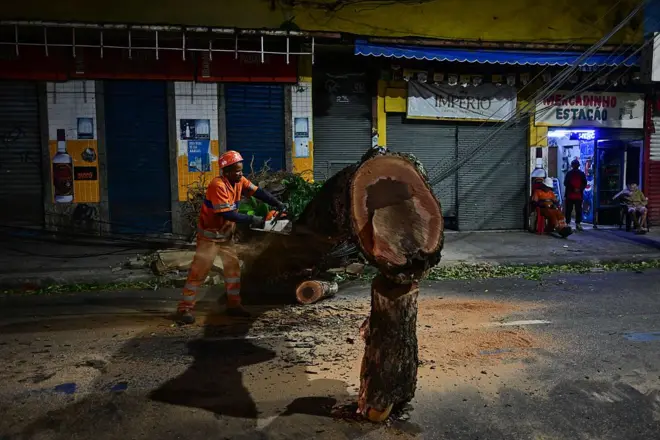 Um funcionário corta uma árvore caída em uma rua residencial após fortes rajadas de vento associadas à chegada de uma frente fria no Rio de Janeiro, Brasil, em 29 de julho de 2026