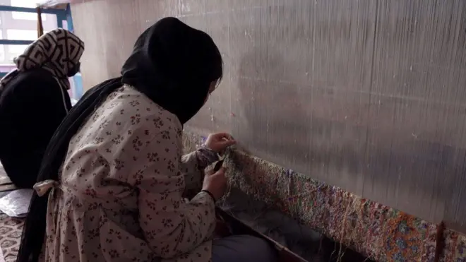 شابتان تجلسان أمام نول، لنسج سجادة كبيرة