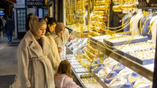 Bir kuyumcunun camından altınlara bakan üç kadın ve bir küçük çocuk