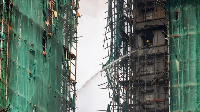 2025年11月27日，香港大埔区宏福苑，一名消防员正用水枪扑灭仍在燃烧的住宅大楼。