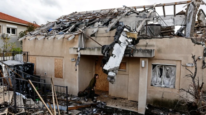 امرأة تحتمي بمدخل بيت تعرّض للقصف