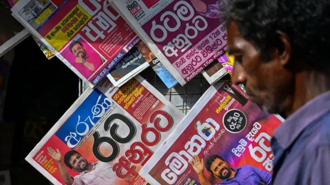 2024 සැප්තැම්බර් 23 වන දින කොළඹදී, රටේ ජනාධිපතිවරණ ප්රතිඵලවල මුල් පිටු සහිතව විකිණීමට තබා ඇති ශ්රී ලාංකික පුවත්පත් සහිත කුටියක් පසුකර යන මිනිසෙක්.