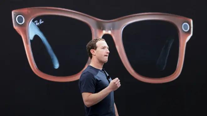 Meta CEO Mark Zuckerberg on a stage describing Meta's Ray-Bans, a large image of which is being shown behind him.