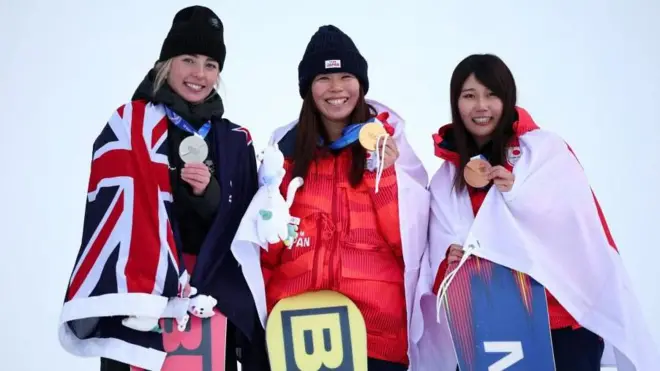 3人が横並びに立ち、首からかけたメダルを左手で胸の前に持ち上げながら笑顔を見せている。それぞれ国旗を肩からかけている