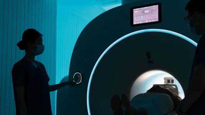 Stock image of a female nurse pressing a button on an MRI machine. 