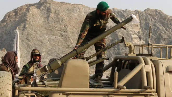 جنود من طالبان يرتدون ملابس عسكرية يغلب عليها اللون الأخضر، يقومون بتحميل قاذفة صواريخ في مركبة عسكرية. وتظهر الجبال في الخلفية.