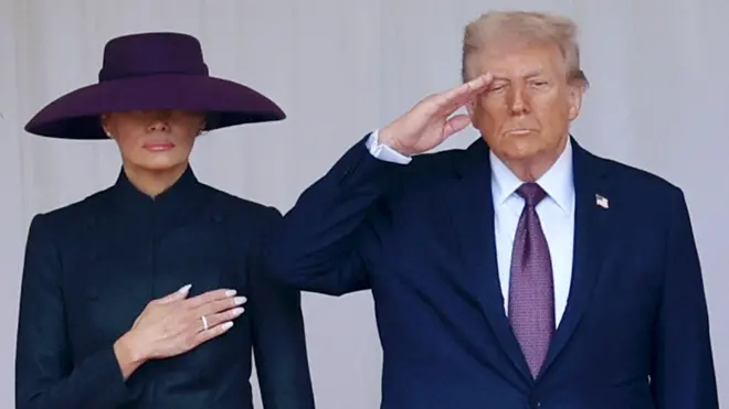 Дональд Трамп у синьому піджаку на фіолетовій краватці тримає руку біля скроні, Меланія у закритій темній сукні та фіолетовому капелюсі, що закриває очі, тримає руку на серці