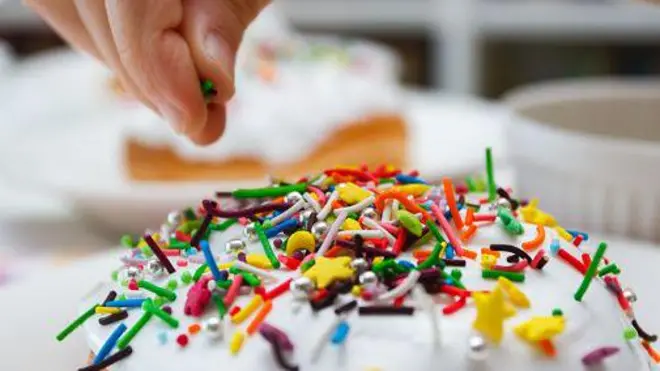 Верхівку паски людина посипає кольоровим декором. 