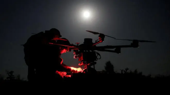 Двое военных готовят к запуску дрон. Ночь, светит луна
