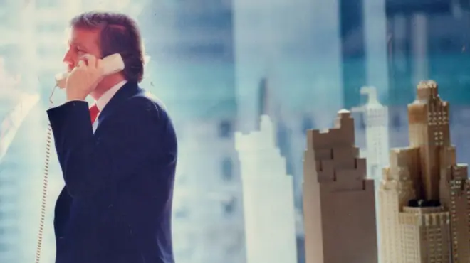 دونالد ترامب يجري مكالمة هاتفية في مكتبه في مانهاتن عام 1987. بجانبه نموذج لبناء ناطحة سحاب.