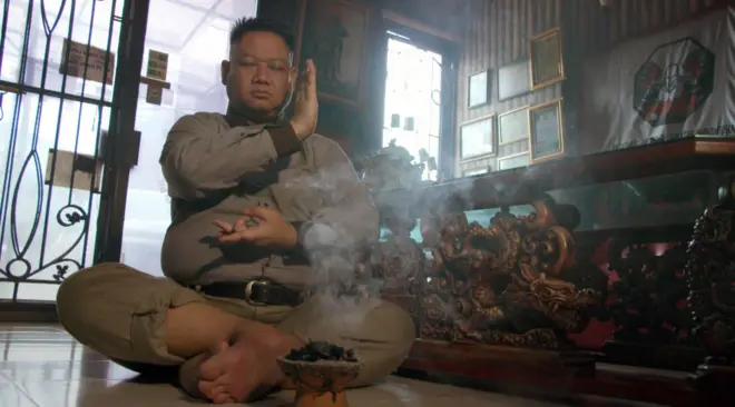 Ki Kusumo sitting cross-legged next to incense bowl