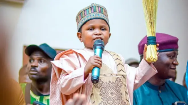 Mahmoud Sadis Buba hold mic for one hand and broom for anoda hand