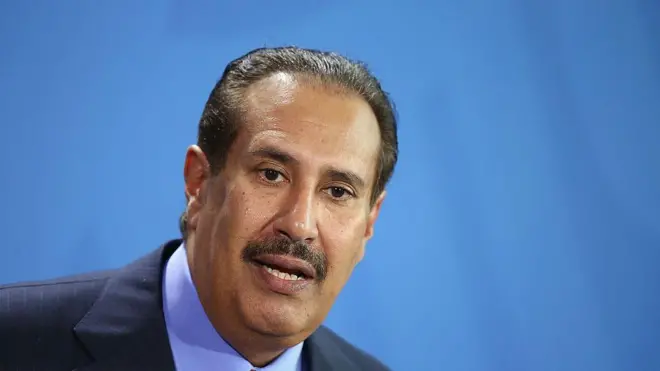 رئيس الوزراء القطري السابق، حمد بن جاسم بن جبر آل ثاني يرتدي سترة زرقاء وقميصاً أزرق يشبه لون السماء وسترة عنق برتقالية اللون.