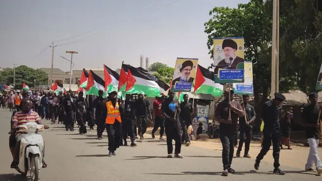 Ndị na-eme ngagharịiwe na-aga ije n'ahịrị ma yiri uwe oji ma jiri ọkọlọtọ mba Iran nakwa foto onyendu kachasị elu na Iran e gburu egbu, Ayatollah Khamenei.